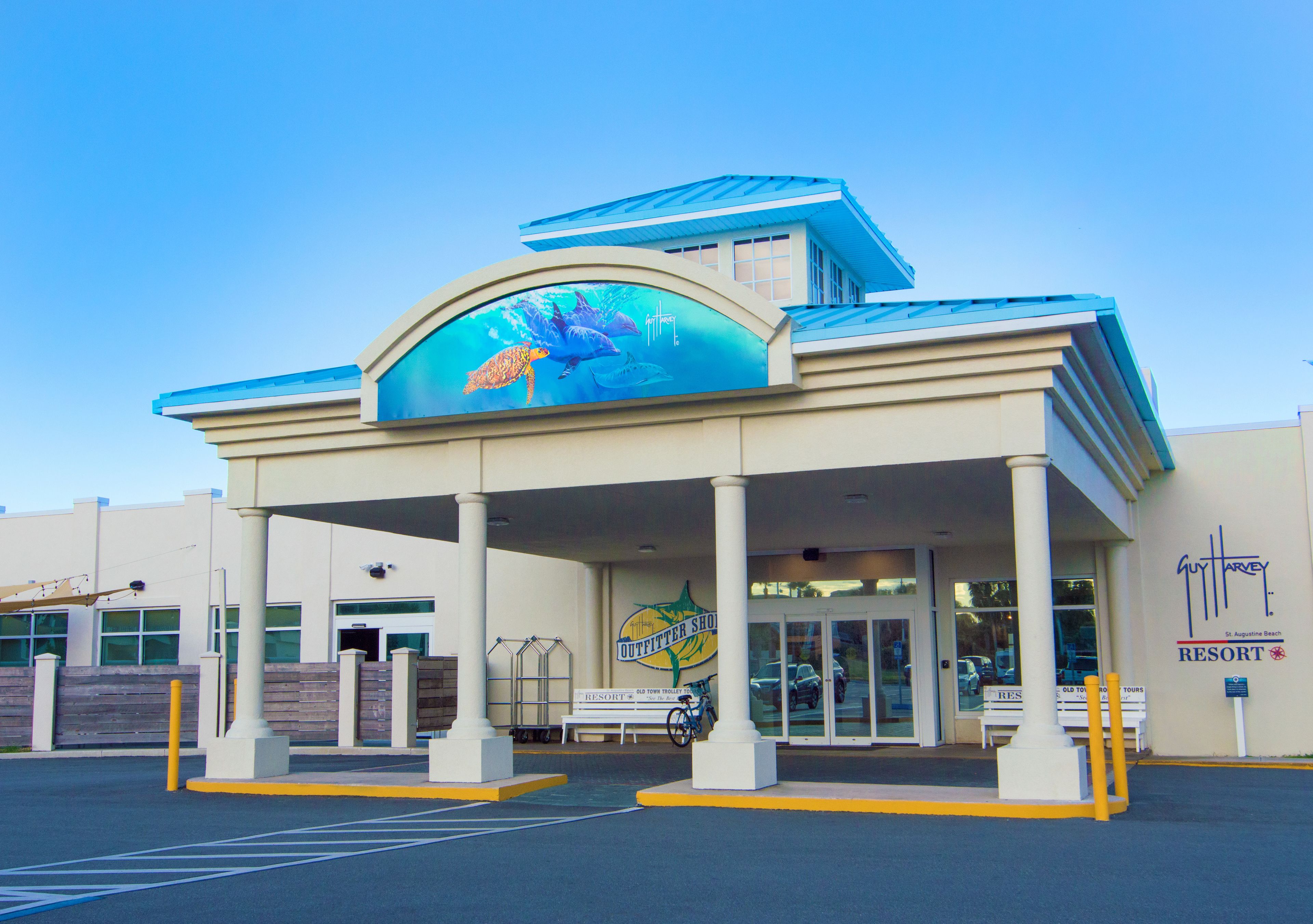 A building with a large mural of marine life on the facade, a covered entrance area, and a sign for 'Guitar Resort'.