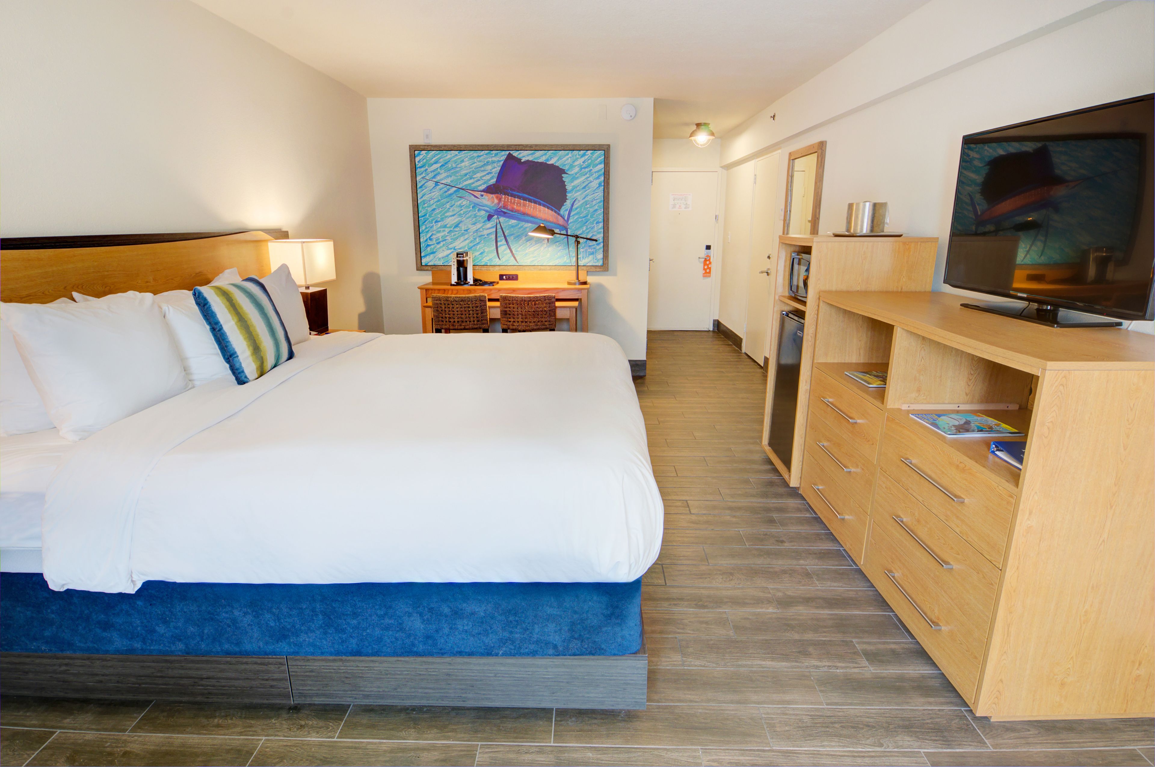 A hotel room with a large bed, a desk with two chairs, a television, and a painting on the wall.