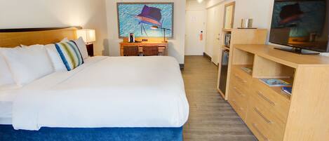 A hotel room with a large bed, a desk with two chairs, a television, and a painting on the wall.