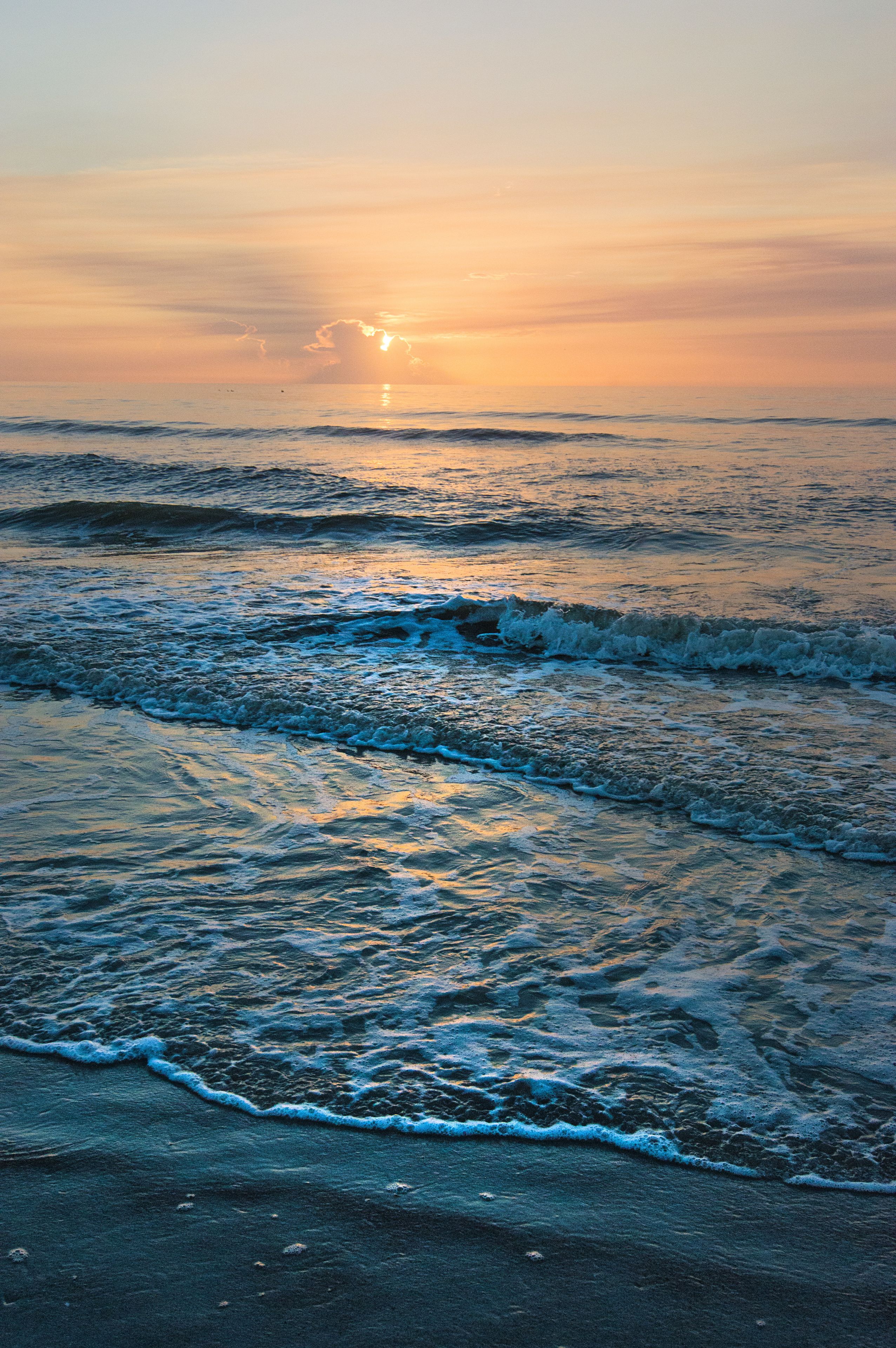 A beach with waves and a sunset.