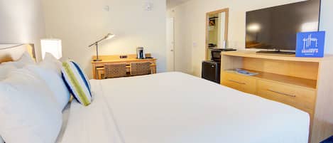 A hotel room with a large bed, a desk with a computer, a flat-screen TV, and a coffee maker.