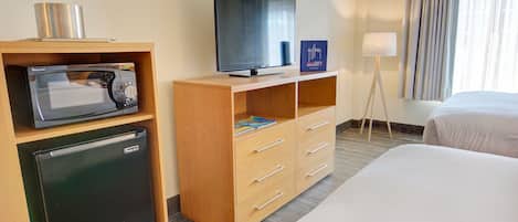 A hotel room with a bed, a TV, a mini-fridge, a microwave, a lamp, and a window with curtains.