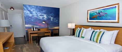A hotel room with a large bed, a desk with a chair, a desk lamp, a wall-mounted TV, and a painting of marine life.