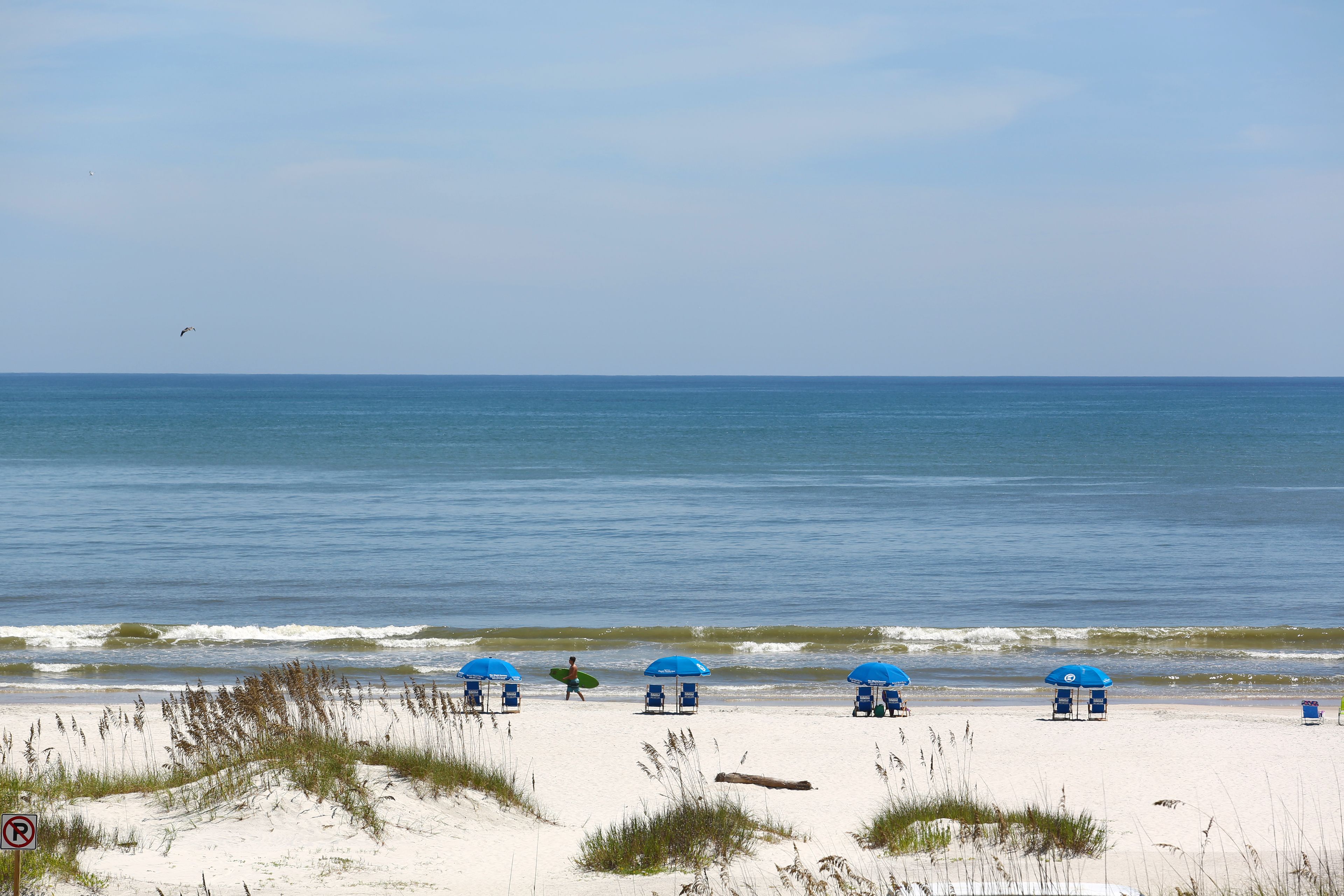 Une plage de sable blanc, des parasols bleus et un ciel dégagé.