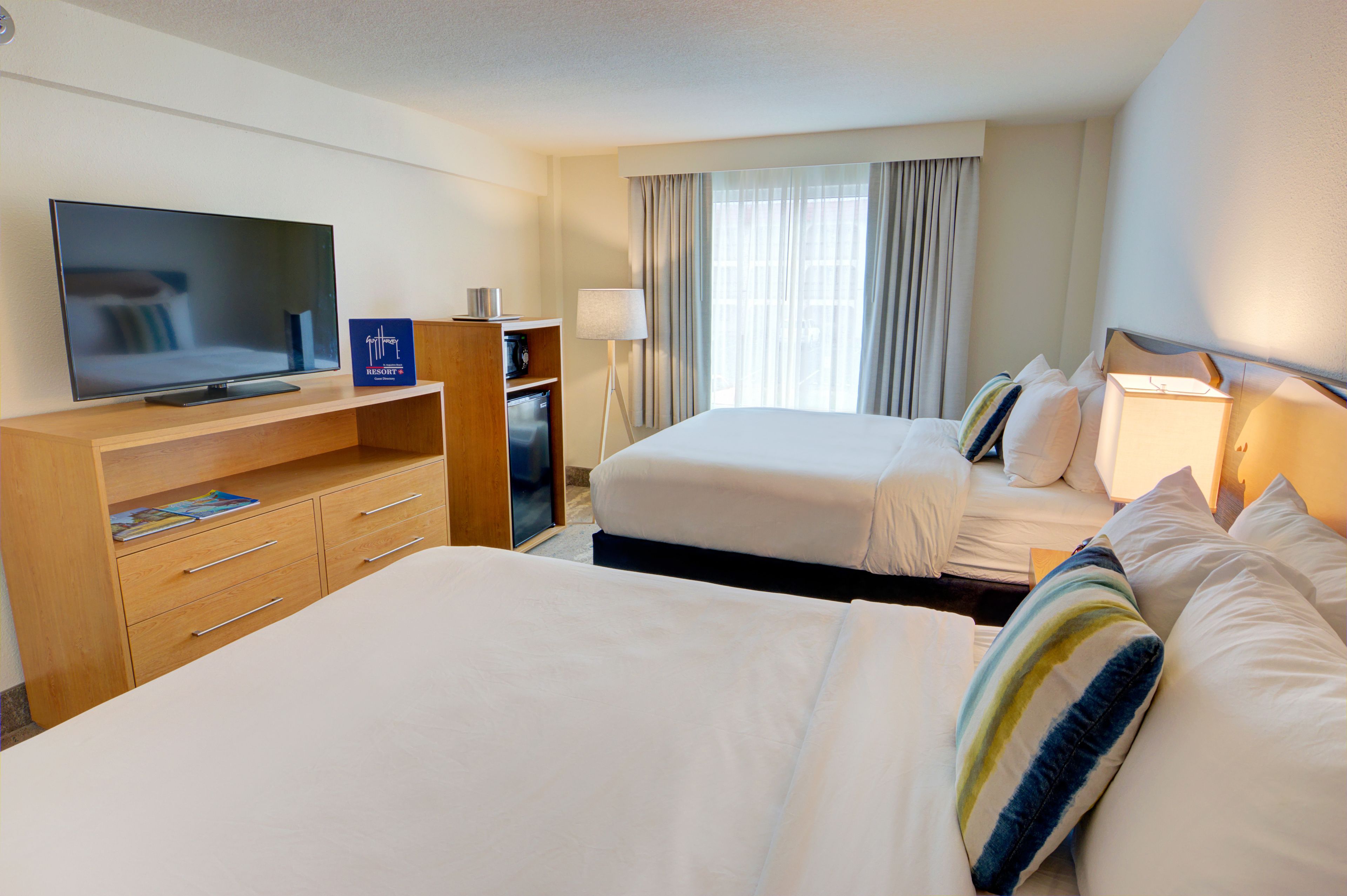 Habitación de hotel con dos camas, televisión, escritorio y lámpara.