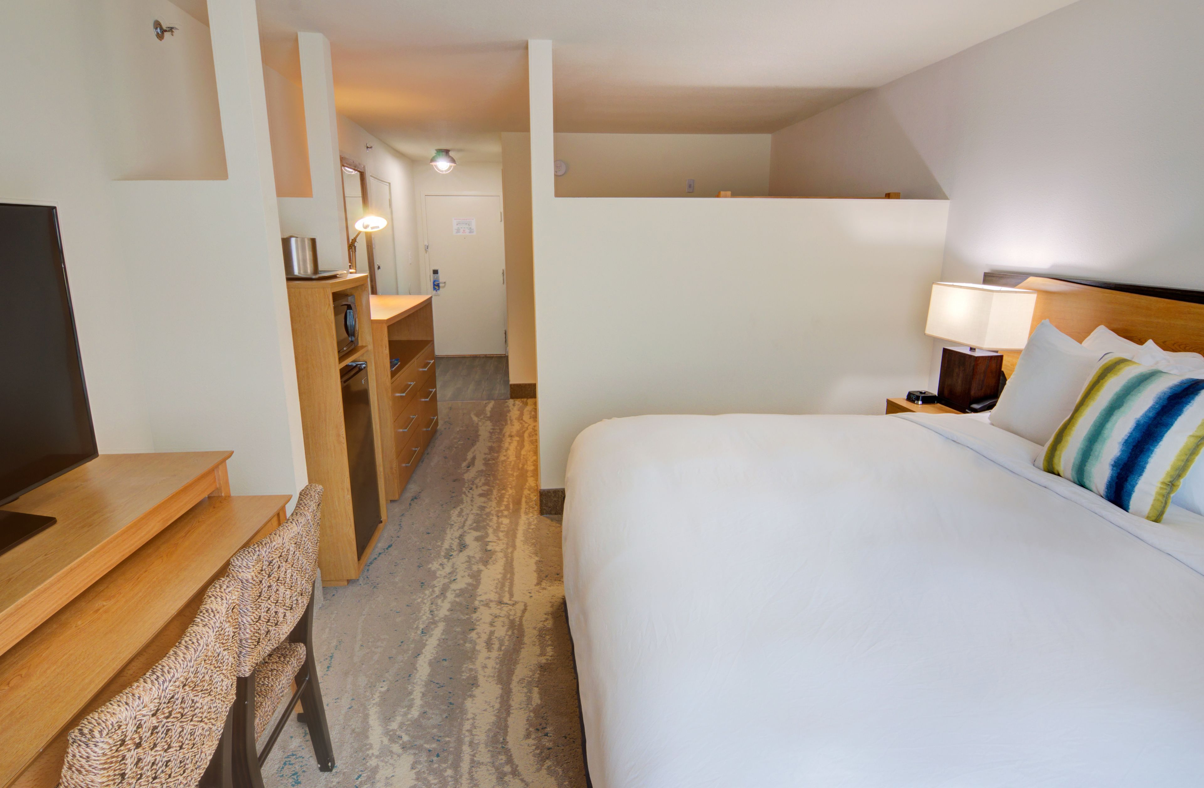 Une chambre d’hôtel avec un lit, un bureau, une chaise, une télévision et une salle de bain visible au fond.