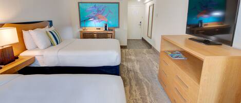 A hotel room with two beds, a desk with a lamp, a TV, and a painting of dolphins.