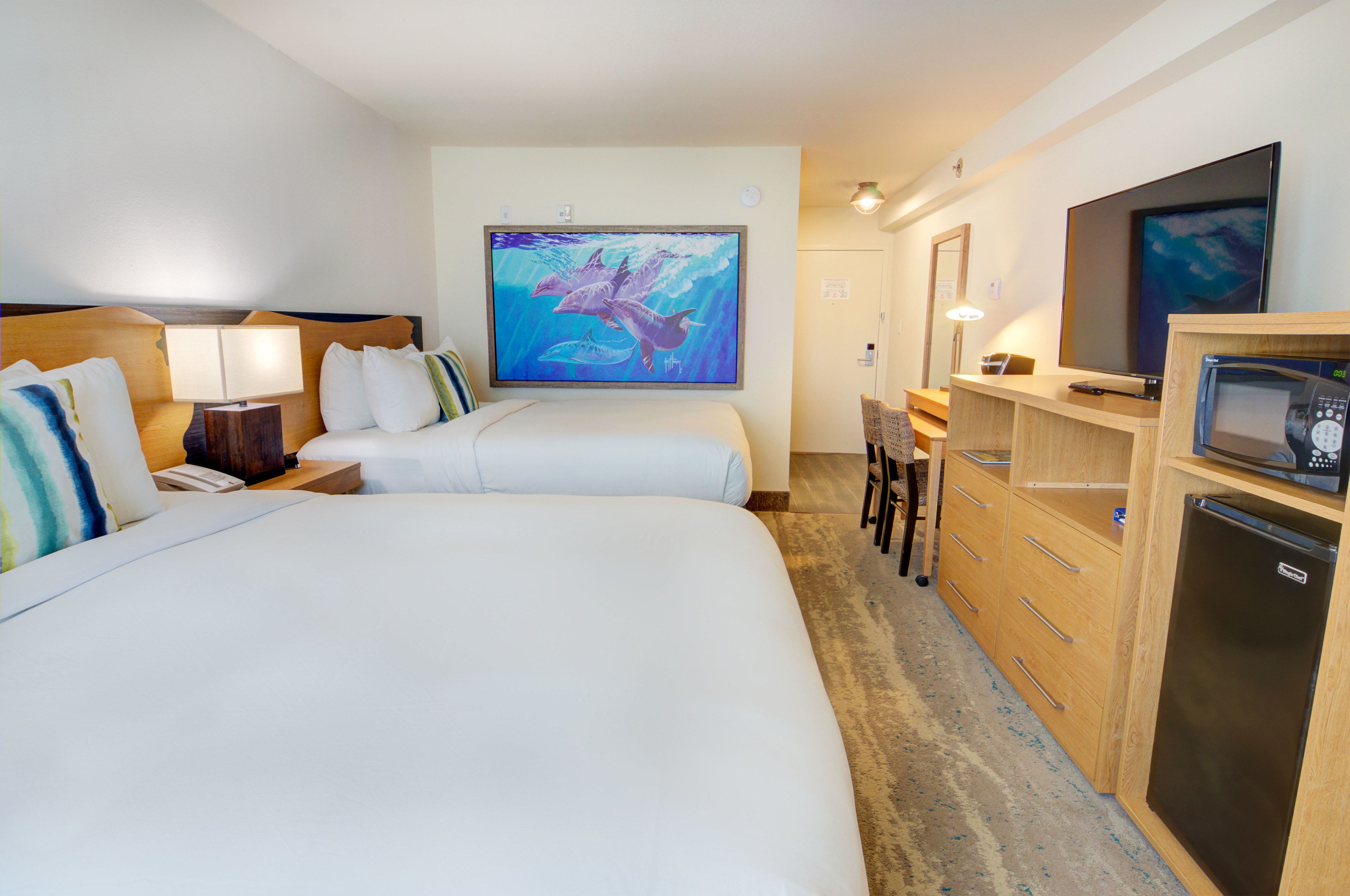 Une chambre d’hôtel avec deux lits, un bureau avec un ordinateur, une télévision et un réfrigérateur.