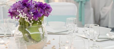 A table set for a formal event with a vase of purple flowers, clear glasses, and scattered candles.