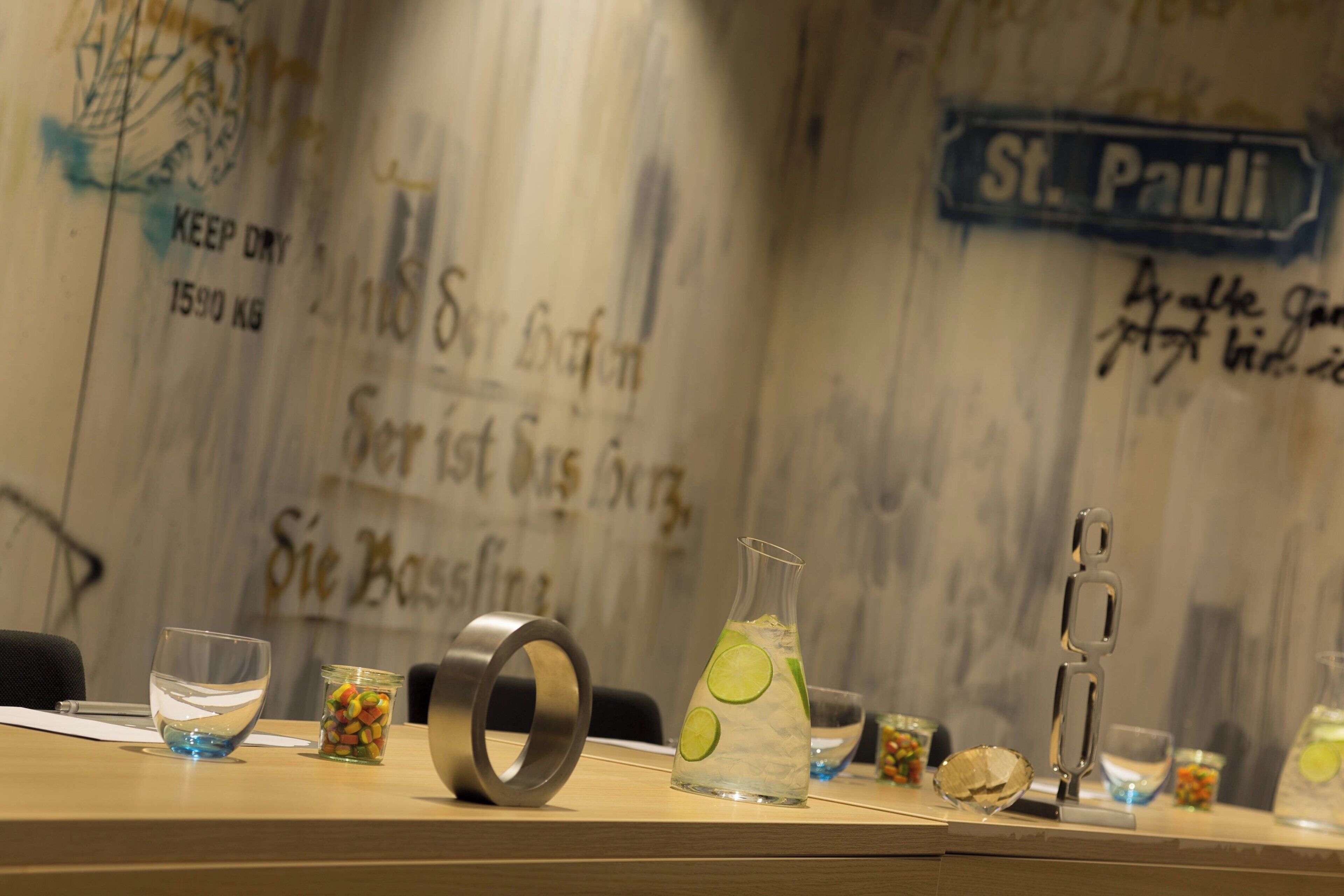 Una zona de bar con mostrador de madera, vasos, una botella y un adorno metálico.