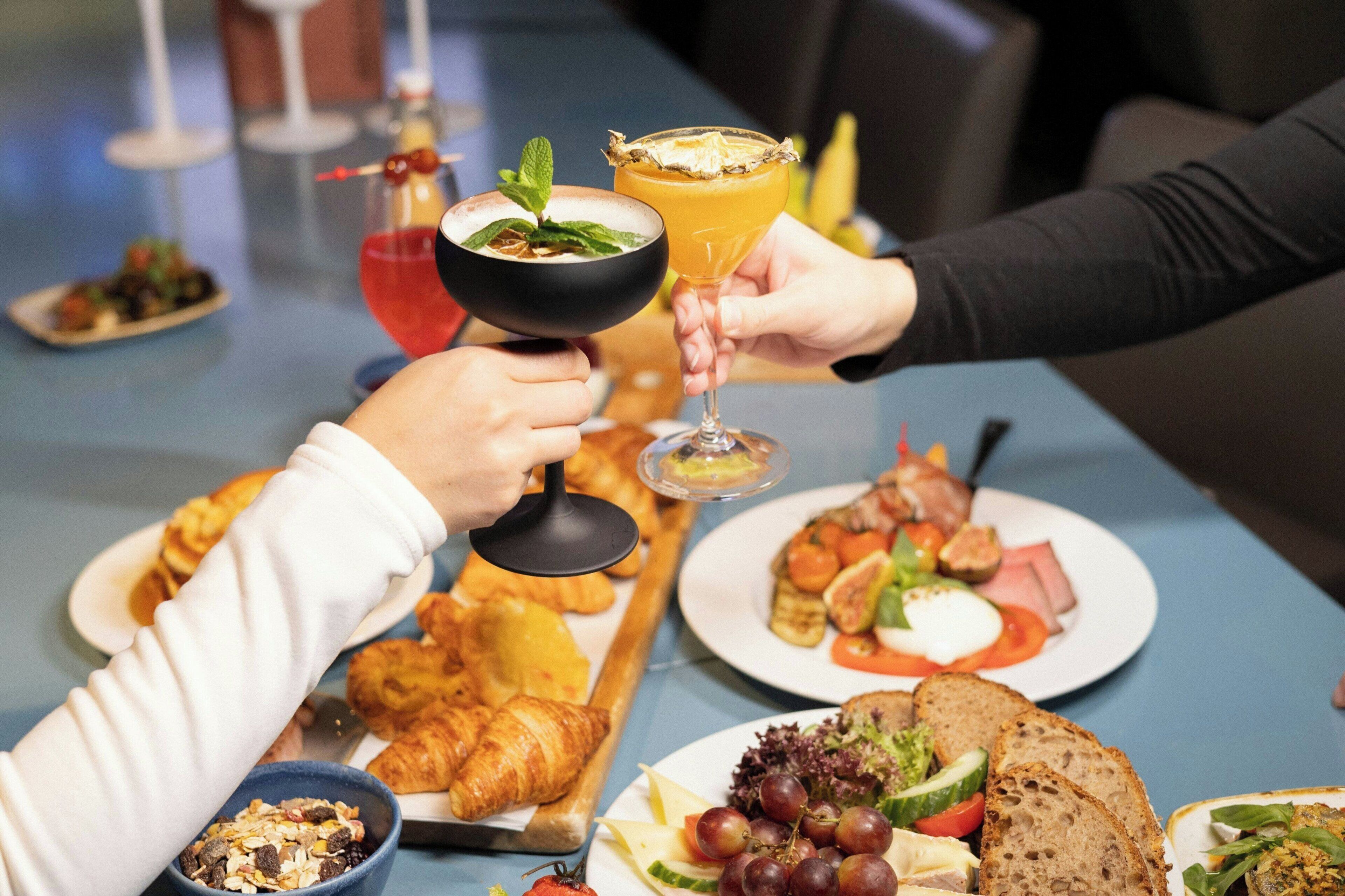 A dining table with various food items and drinks, including a bowl, a glass with a garnish, and plates with different dishes.