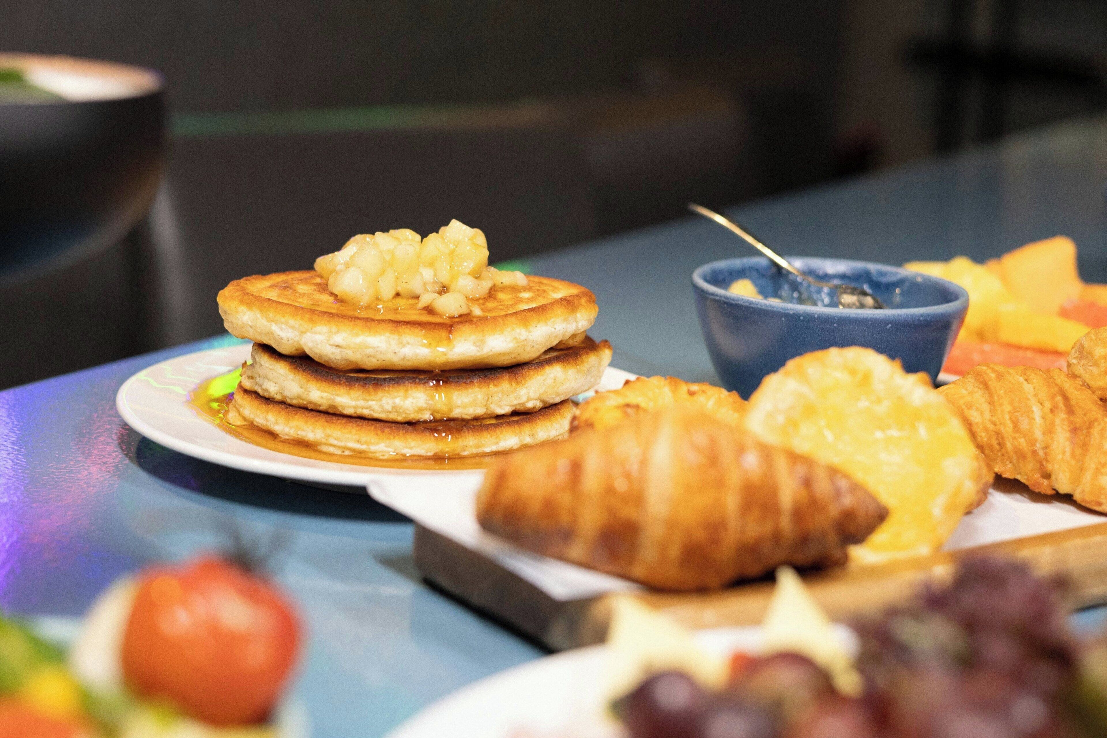 A breakfast plate with pancakes, a croissant, and a bowl of fruit.