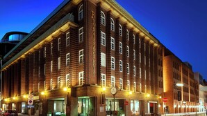 Um edifício histórico de tijolo com vários andares, janelas amplas e uma entrada imponente.