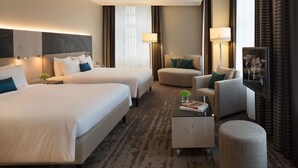 Quarto de hotel com duas camas, um sofá, uma mesa de centro e uma televisão.