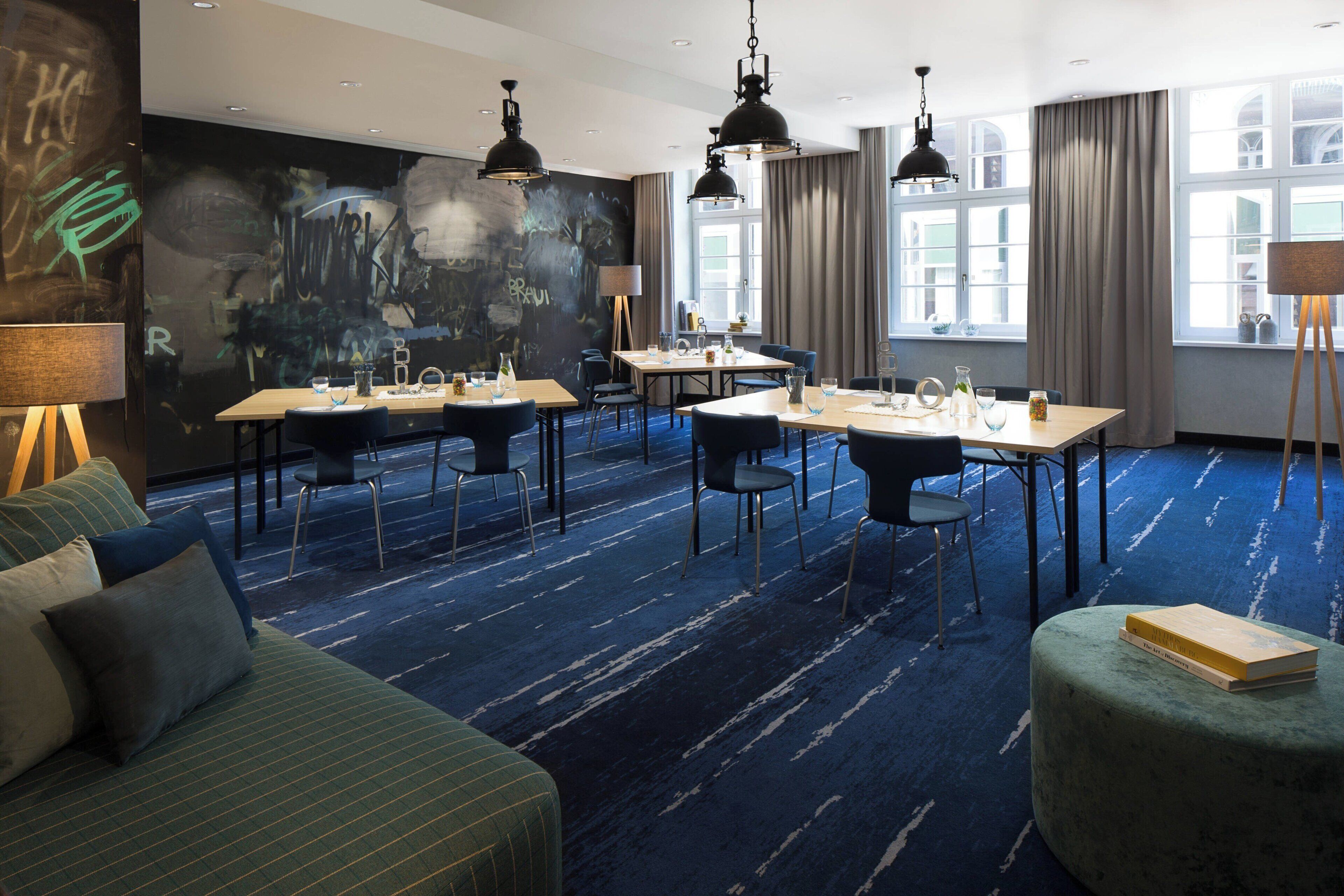 A hotel room with a blue carpet, a green sofa, a wooden coffee table, and a bookshelf.