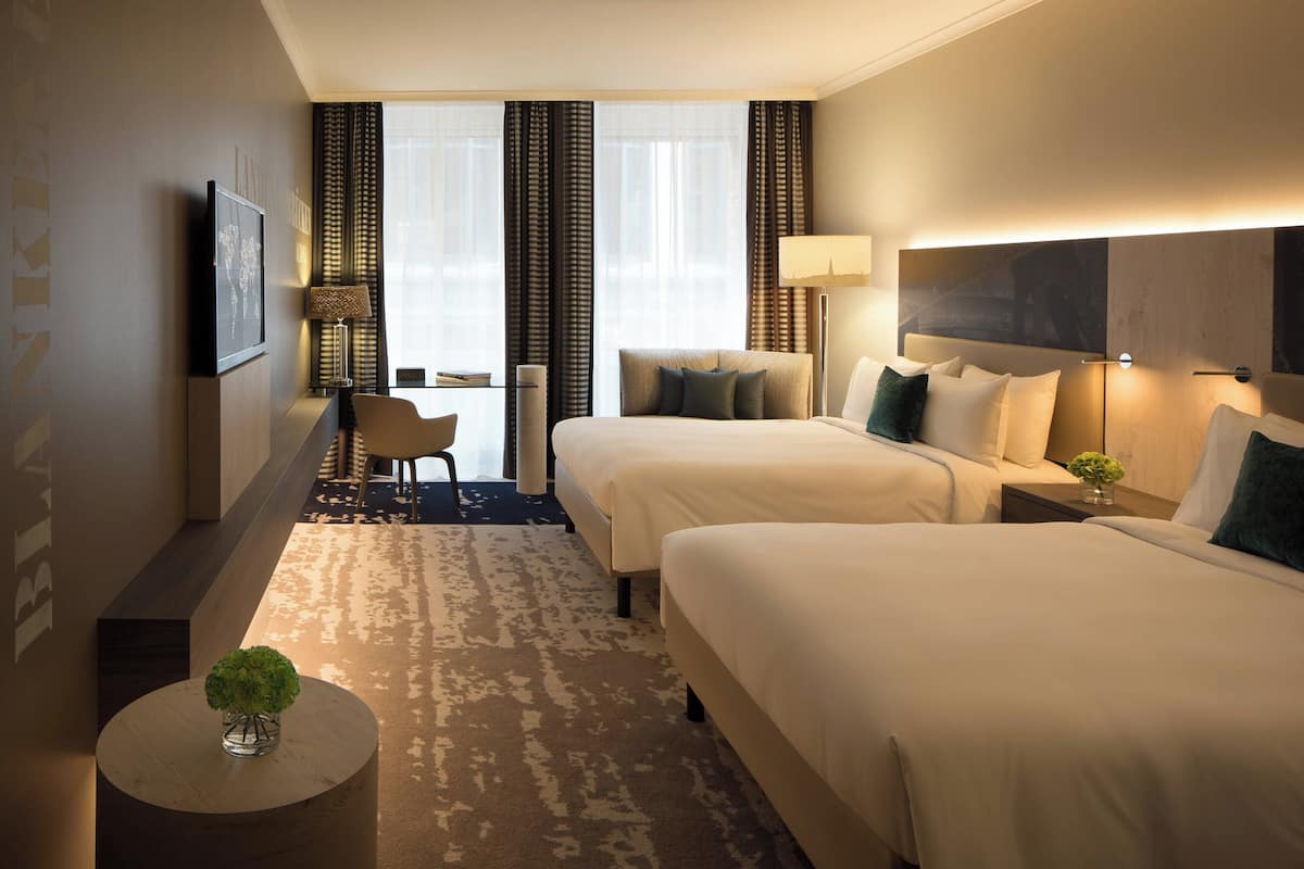 Une chambre d’hôtel avec deux lits, un bureau, une chaise et une petite table sur laquelle est posée une plante.