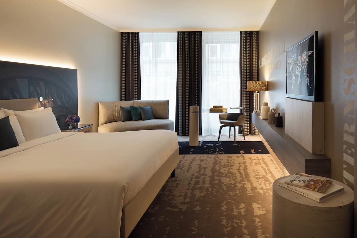 Une chambre d’hôtel avec un grand lit, un canapé, un bureau avec une chaise, une lampe et une carte du monde accrochée au mur.
