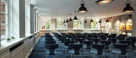 A conference room with rows of chairs, large windows, and pendant lighting.
