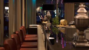 Um lobby de hotel moderno com assentos de couro, área de bar espelhada e iluminação ambiente.