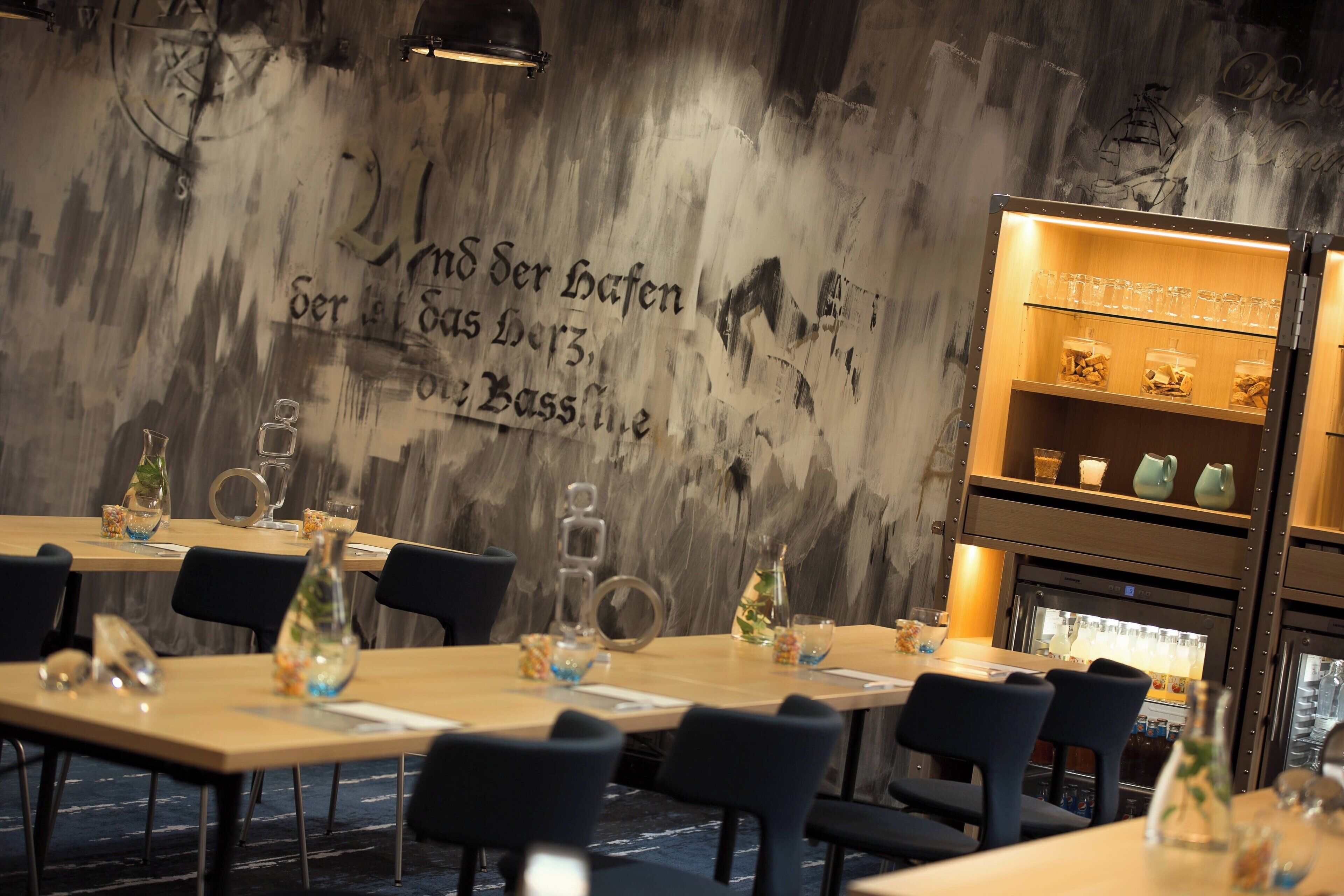 Un interior de restaurante con mesas de madera, sillas negras y una pared con texto en alemán.