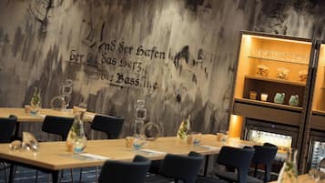 Un interior de restaurante con mesas de madera, sillas negras y una pared con texto en alemán.