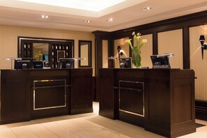 Reception area with two desks, a vase with flowers, and a mirror.