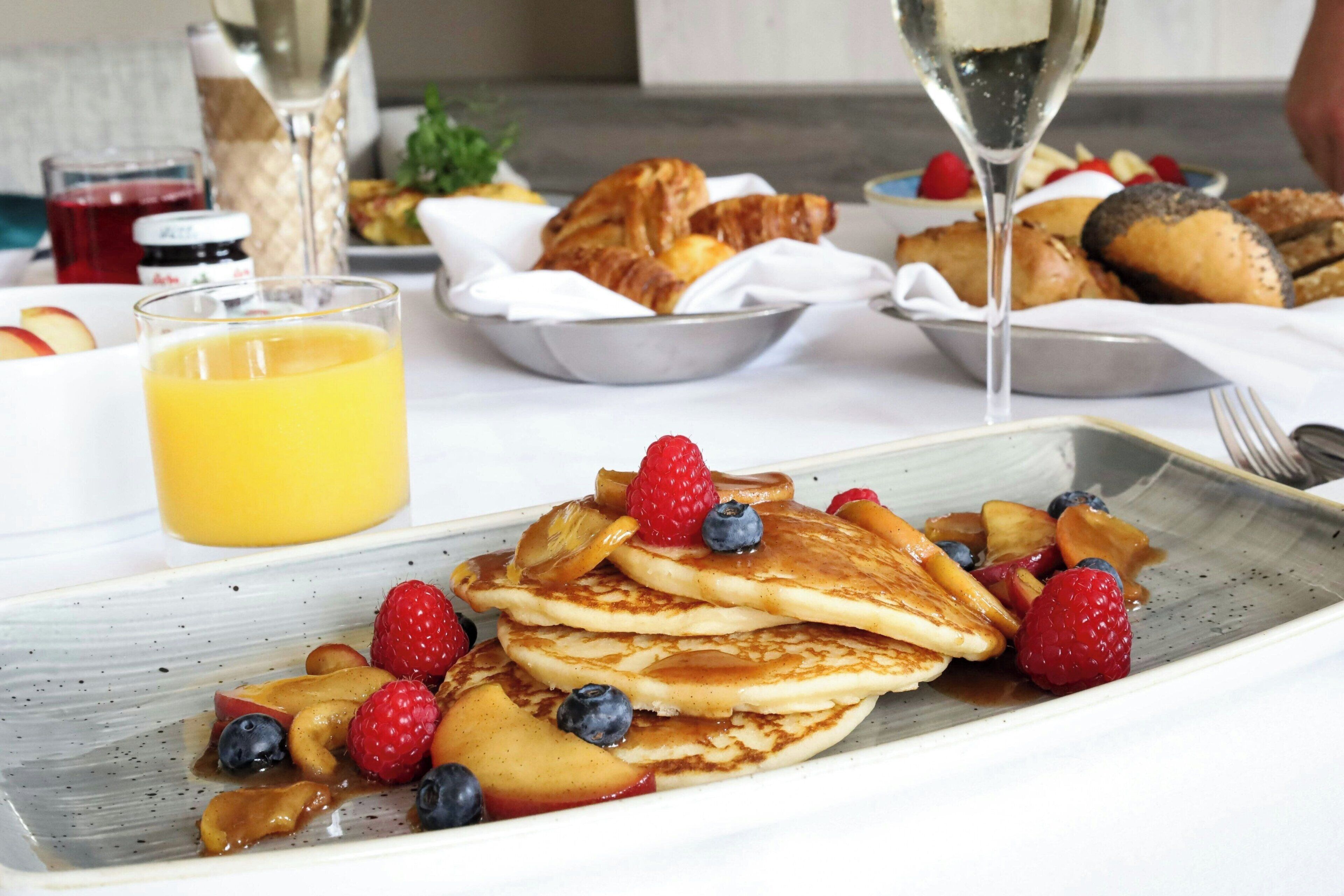 A breakfast setting with pancakes, berries, and a glass of orange juice.