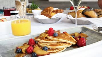 A breakfast setting with pancakes, berries, and a glass of orange juice.