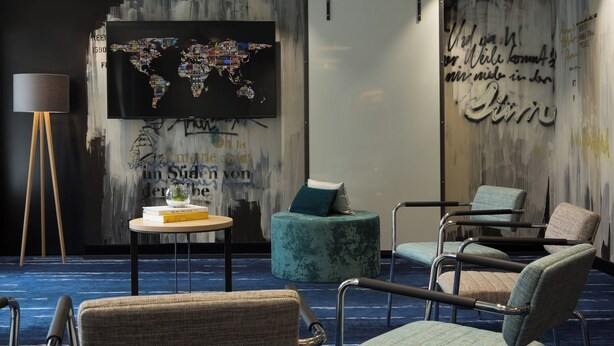 A modern hotel room with a world map artwork, a round table with books, and a blue carpet. - Renaissance Hamburg Hotel (Hamburg)
