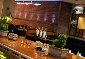 Un espace bar avec un comptoir en bois, des bocaux en verre remplis d’épices, des bougies et un mur de briques en arrière-plan.