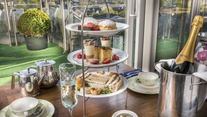A tiered dessert tray with sandwiches and pastries, a champagne bottle, and tea service on a balcony overlooking a green landscape. - Stradey Park Hotel (Llanelli)