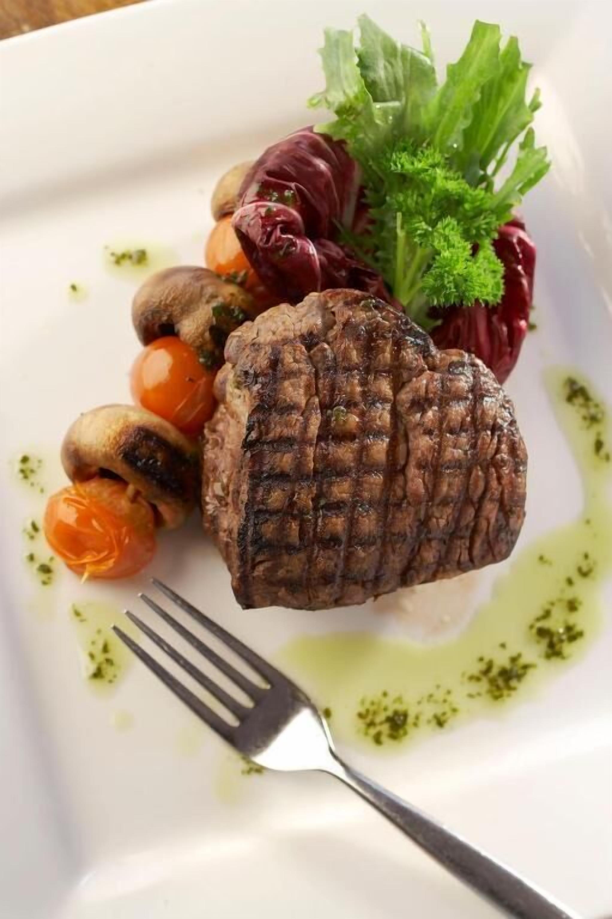 A plate with grilled meat, cherry tomatoes, mushrooms, and a garnish of parsley and red cabbage.