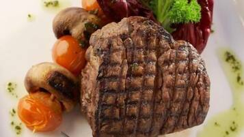 A plate with grilled meat, cherry tomatoes, mushrooms, and a garnish of parsley and red cabbage.