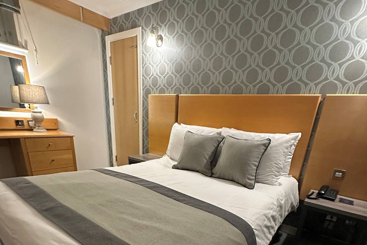 Une chambre d’hôtel avec un lit, une table de chevet, une lampe et un mur décoré d’un motif.