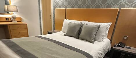 A hotel room with a bed, bedside table, lamp, and a patterned wall.