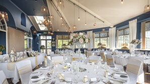 A banquet hall with round tables set for a formal event, featuring white tablecloths, gold sashes, and floral centerpieces. - Stradey Park Hotel (Llanelli)