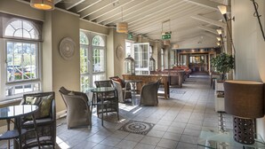 A spacious indoor area with high ceilings, large windows, wicker furniture, and a visible restaurant sign. - Stradey Park Hotel (Llanelli)