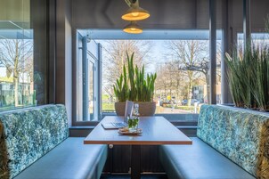 Un espacio de descanso moderno con una mesa de madera, dos bancos acolchados y una planta en maceta.