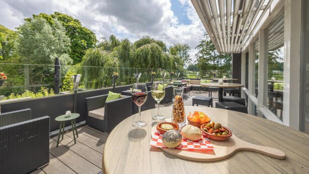 An outdoor patio with round tables, wicker furniture, and a variety of food and drinks.