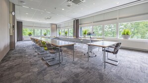 A conference room with a long table, multiple chairs, and large windows with views of greenery.