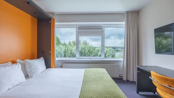 Een hotelkamer met een groot bed, een bureau en een raam met uitzicht op bomen.