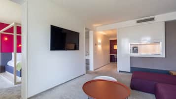 A modern hotel room with a bed, a seating area, and a TV mounted on the wall.