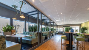 A modern restaurant with long communal tables, booths, and high ceilings with grid patterns.
