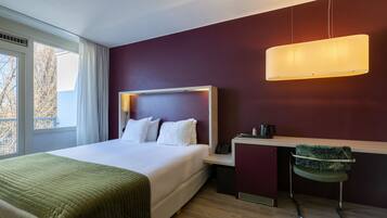 Una habitación de hotel moderna con una cama grande, un escritorio, una silla y un ventanal con cortinas.