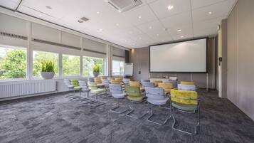 A conference room with rows of chairs, a projector screen, and large windows with plants.