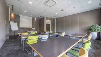 Ein Konferenzraum mit großem Tisch, mehreren Stühlen, einer Tafel und einer Uhr an der Wand.
