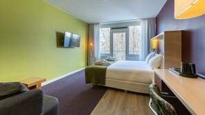 A hotel room with a bed, a desk, a chair, a television, and a window with curtains.