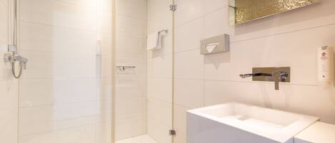 A modern bathroom with a glass-enclosed shower, a white sink, and a mirror with a gold frame.