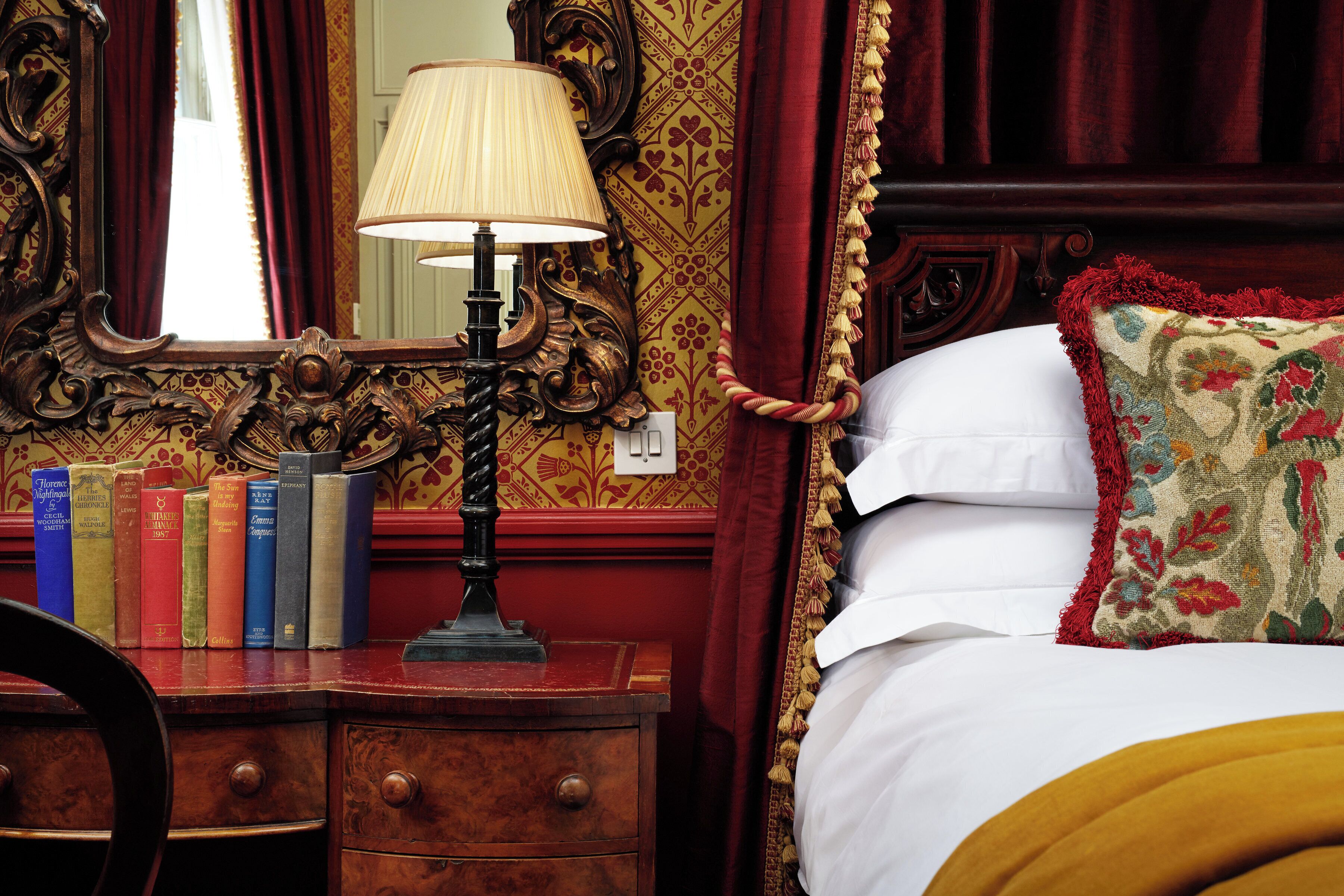 A bedroom with a wooden dresser, a mirror, and a lamp. There are books on the dresser and a bed with a floral pillow.