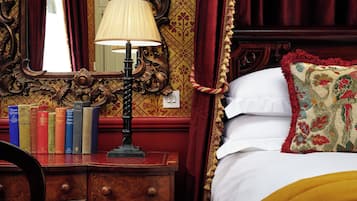 A bedroom with a wooden dresser, a mirror, and a lamp. There are books on the dresser and a bed with a floral pillow.